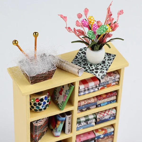 Close-up of fabric storage shelf with colorful fabrics and decorative elements in Tailor Shop Miniature Dollhouse.