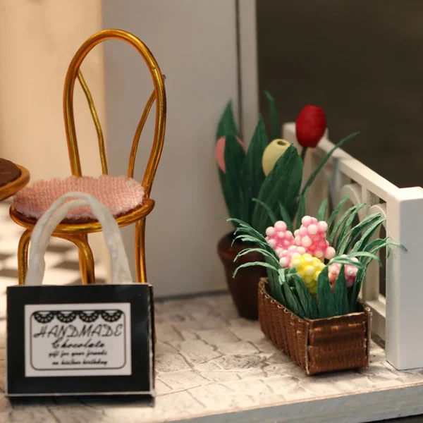 Close-up of a cozy outdoor seating area at the Cocoa Fantasy shop, featuring a chair, a shopping bag labeled "Handmade Chocolate," and a basket of colorful flowers.