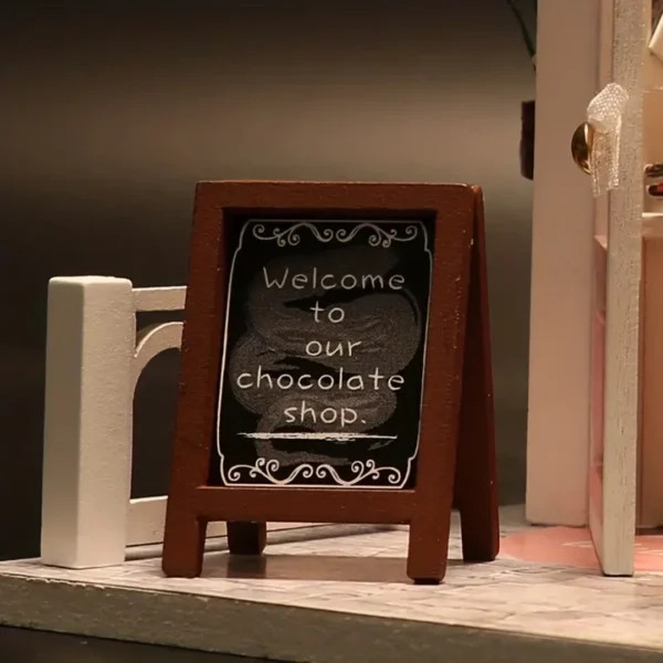 Close-up of a miniature blackboard sign with the words "Welcome to our chocolate shop," placed outside the entrance of the Cocoa Fantasy chocolate shop.