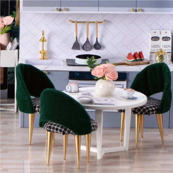 Close-up of a modern miniature dining room with green velvet chairs, a white round table with pink roses, and a kitchen backdrop in the Cozy Time DIY miniature dollhouse.