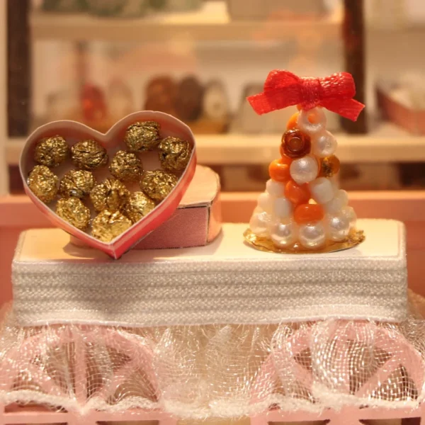 Close-up of a miniature dessert cart with a heart-shaped chocolate box and a sweet treat tower, detailed with golden chocolates and decorative elements.