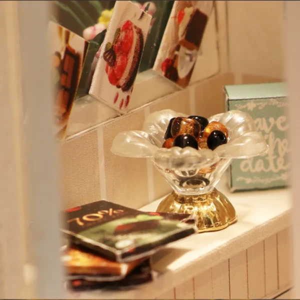 Close-up of a glass dish filled with chocolate candies and chocolate bars in a miniature chocolate shop scene.