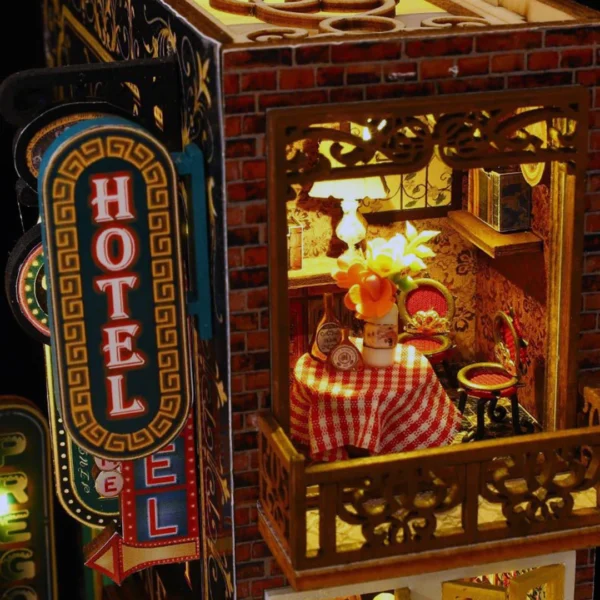 Close-up view of a cozy balcony with a table set featuring a red checkered tablecloth, flowers, and warm lighting in the Scarbrough Hotel miniature dollhouse kit.