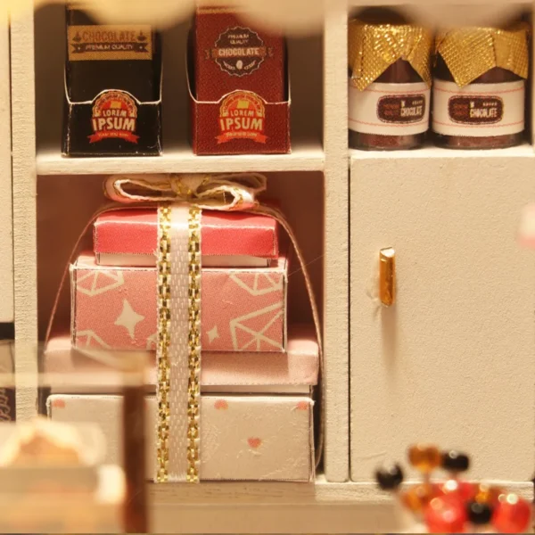 Close-up of miniature dessert gift boxes with pink and gold wrapping displayed on a shelf in a chocolate shop.