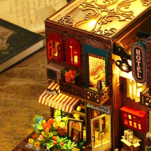 Close-up of the flower shop and part of the hotel from the Scarbrough Hotel DIY miniature dollhouse kit, showing detailed flowers, an awning, and illuminated windows.