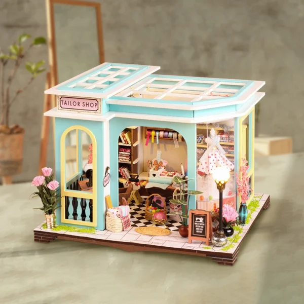 A side view of a cozy tailor shop miniature dollhouse kit, featuring a stylish exterior with a welcoming entrance, vibrant flowers, and a "Tailor Shop" sign above the door.